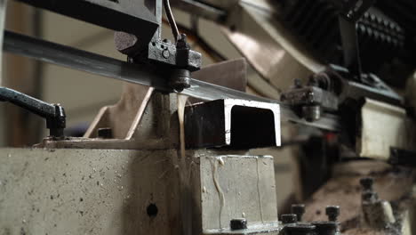 metal cutting bandsaw slicing through a steel beam in an industrial workshop, coolant dripping on blade