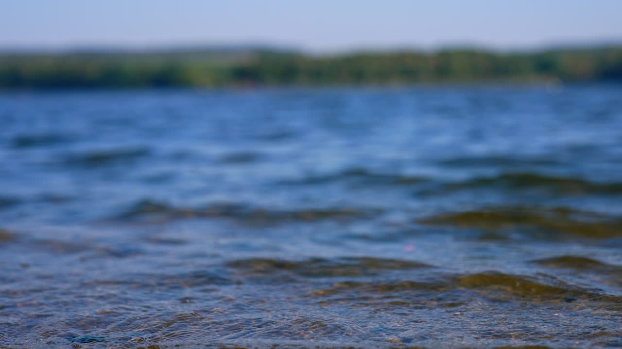 Little waves on the river on sunny daytime. Close up view on the water of the lake on windy day. Blurred backdrop.