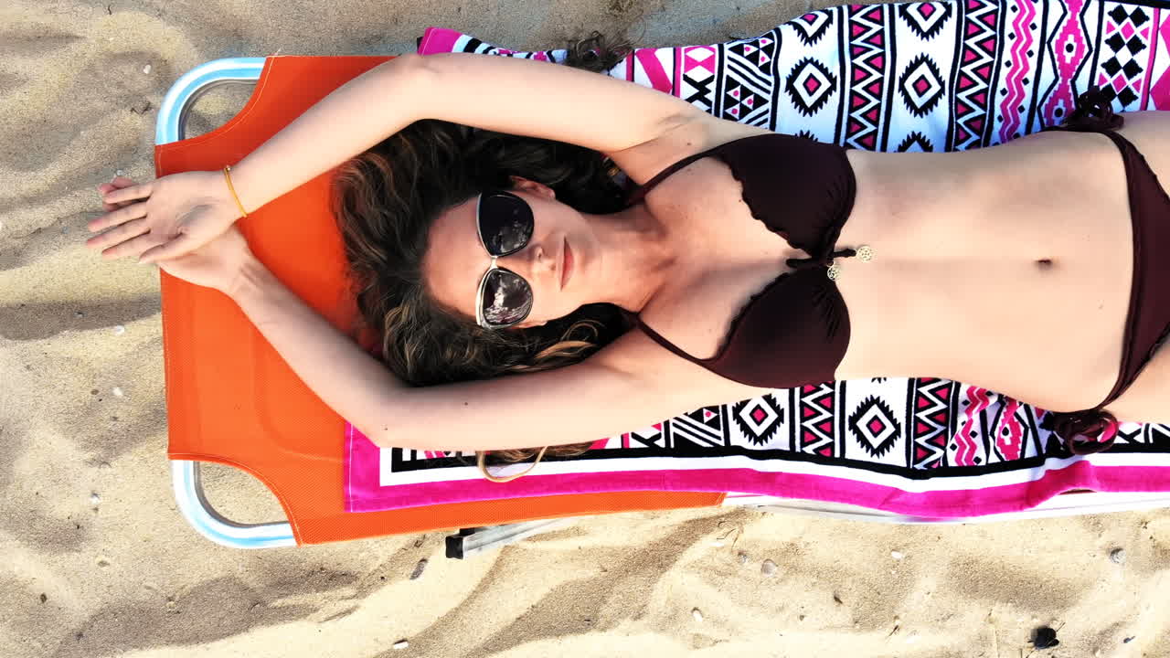 Top view of a woman laying on sunbed, relaxing and looking up