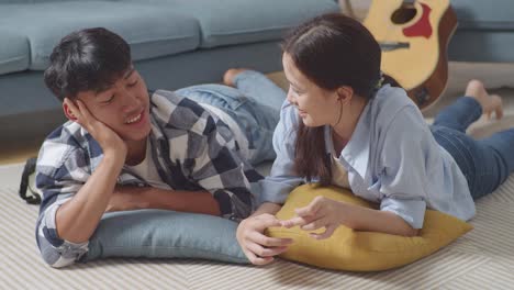 asian teen couple speaking, laughing, and enjoying time together while lying on carpet on the floor at home