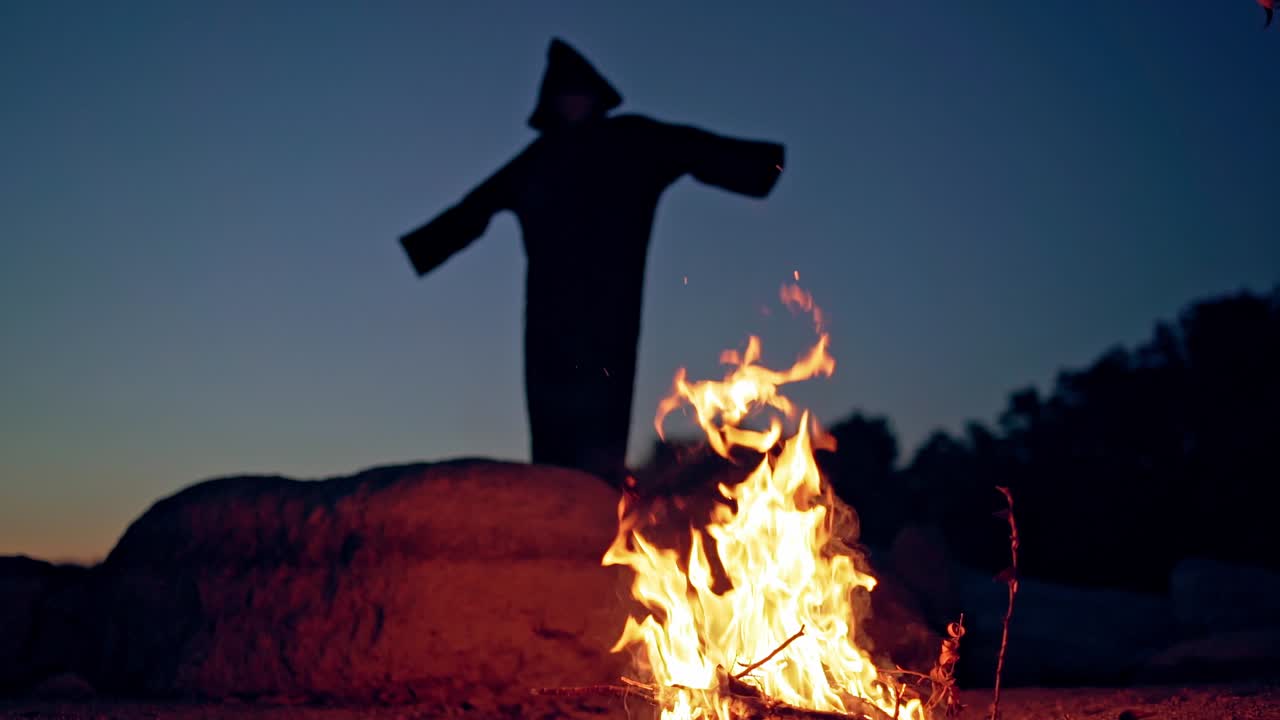 Witch by night fire in forest. Witch silhouette hexing in dark forest
