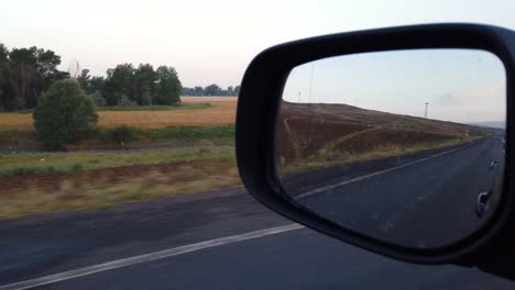 Reflection-side-rear-view-car-mirror-in-the-morning-on-the-road-at-sunset-or-sunrise