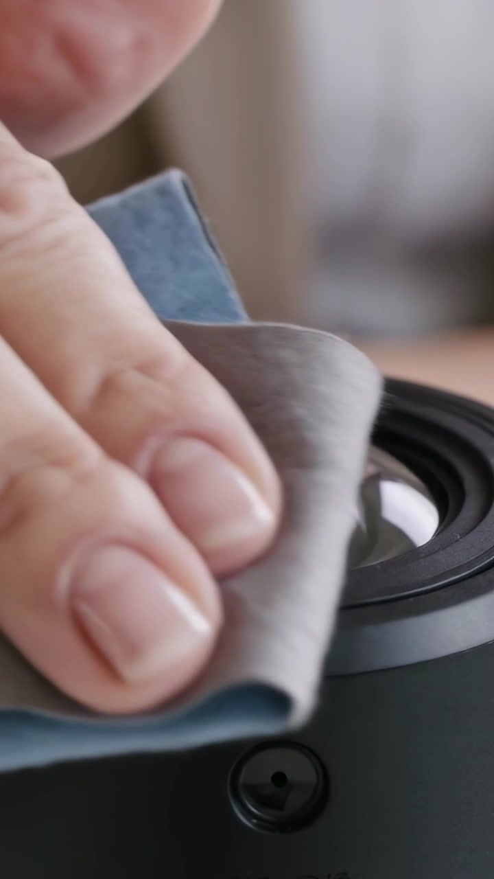 Vertical video: Bringing microfiber cloth down, hand wiping convex camera lens in room, cleaning