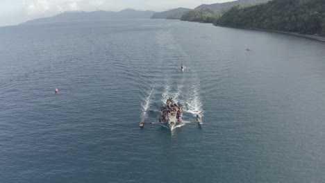 aerial footage of a big running fishing boat with a lot of local fishermen onboard on a turquoise blue water on a tropical island in the philippines