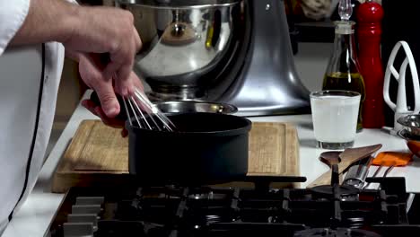 a chef skillfully prepares a sauce in a state-of-the-art kitchen. utilizing a whisk, the chef blends ingredients in a black saucepan while various kitchen tools are nearby