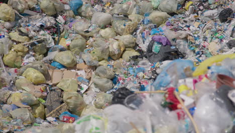 Huge-pile-of-plastic-garbage-bags-at-outdoor-recycling-plant,-slow-pan