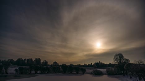 winter moonrise timelapse through clouds over countryside landscape. overcast weather in snowy winter landscape with frost on trees and snow on the ground