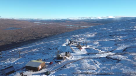 Glencoe-Mountain-Resort-with-sparse-snow-cover,-contrasting-with-the-surrounding-Scottish-Highlands,-aerial-view