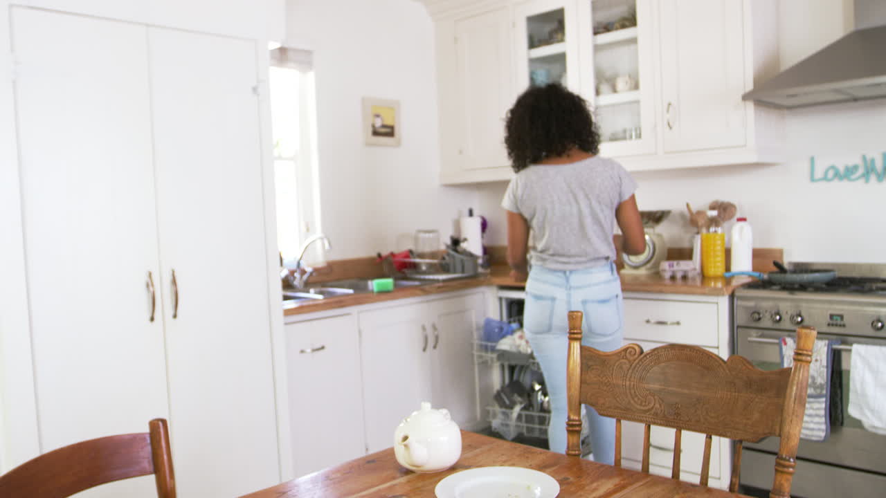 Adolescente che schiarisce il tavolo della colazione e che carica la lavastoviglie