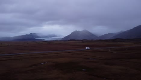 an expansive aerial shot captures a motorhome traveling along a road that cuts through a vast, rugged, and open icelandic landscape