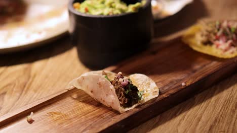 a hand assembles a taco on a wooden board in warm lighting, capturing the essence of mexican cuisine