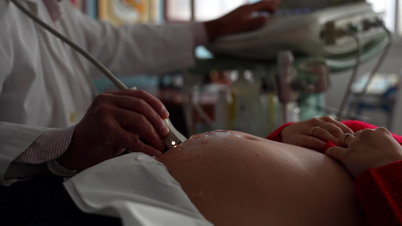 el vientre de la mujer embarazada respira profundamente mientras el ginecólogo lo escanea.