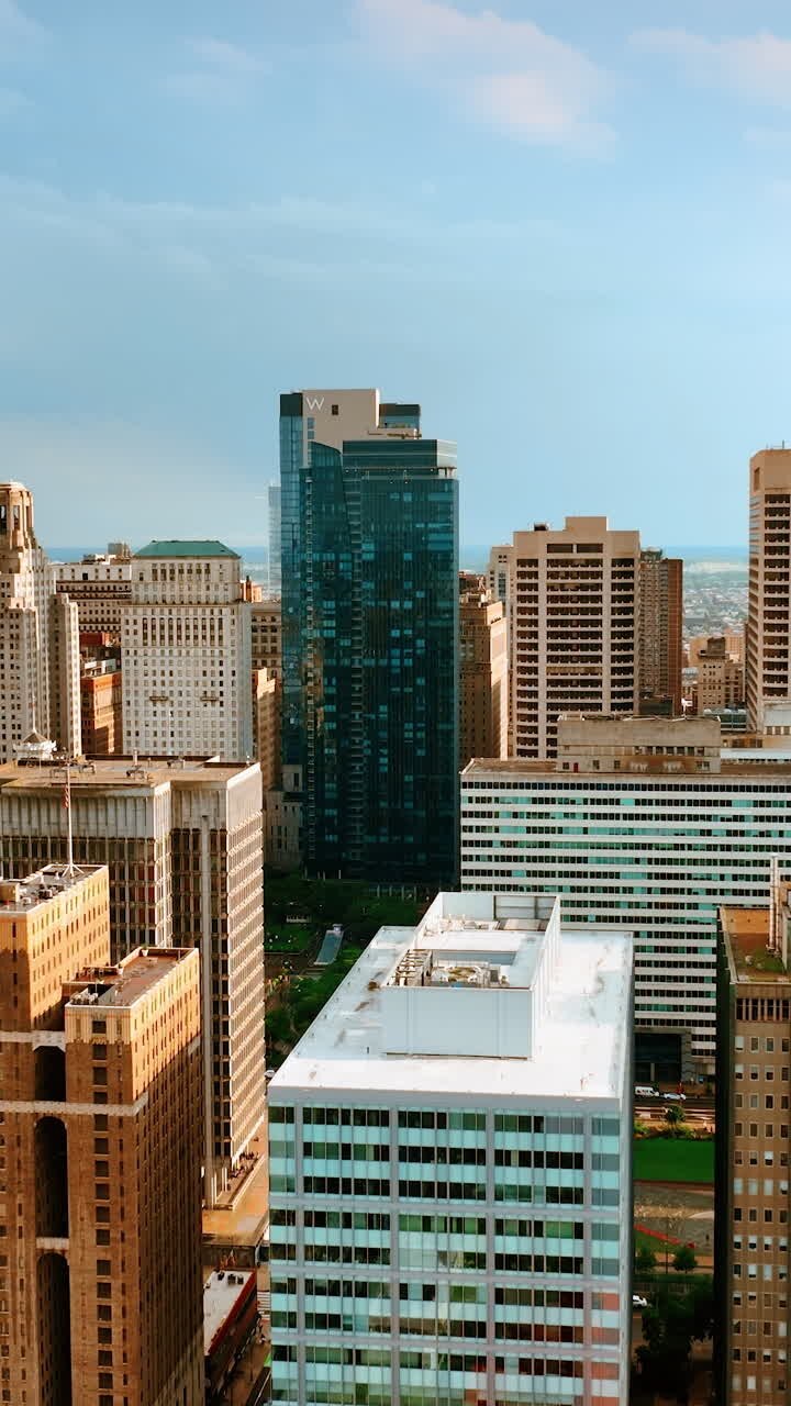 Tops of skyscrapers towering above multi-storied buildings. Drone footage slowly rising above Philadelphia cityscape. Vertical video
