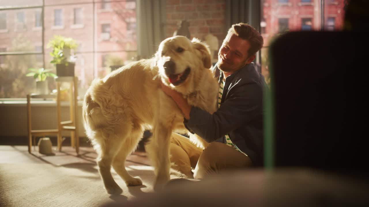행복한 잘생긴 젊은이가 집에서 개와 놀고, 화려한 골든 리트리버, 바닥에 앉아 놀리고, 애정하고, 흥분한 개를 고, 세련된 아파트에서 재미있게 놀고.