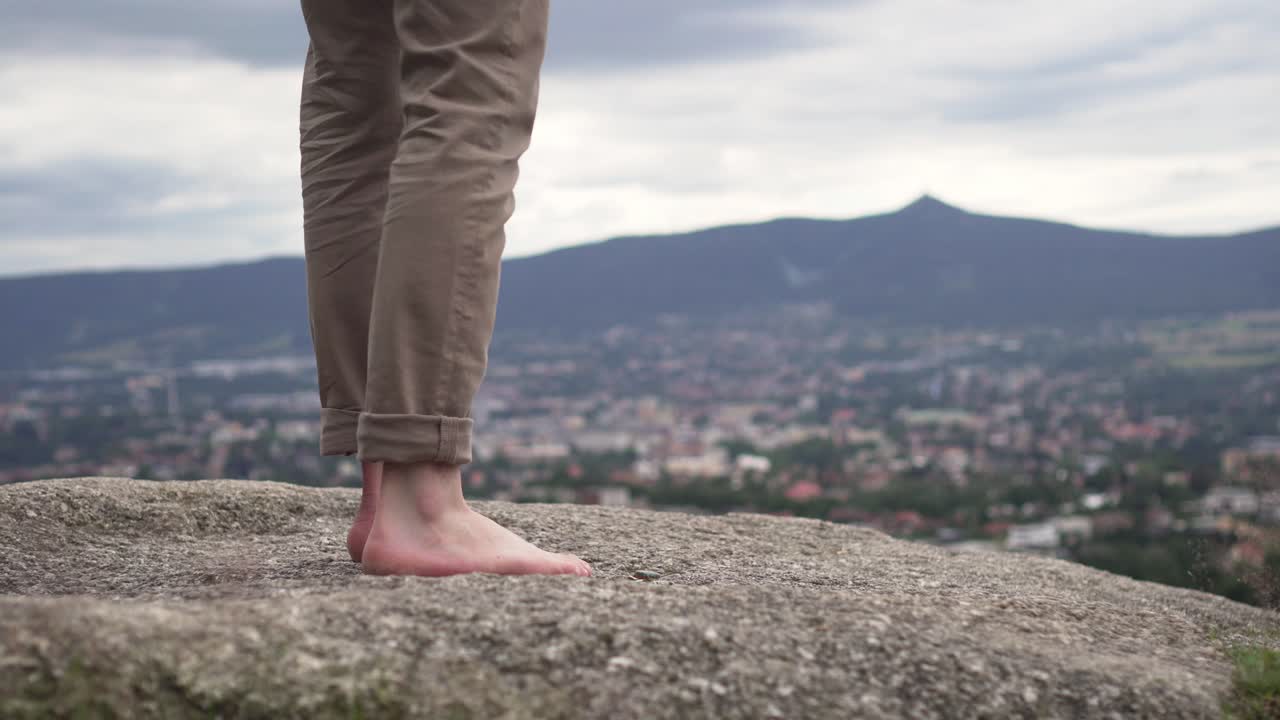 primer plano de pies descalzos masculinos caminando y parados sobre una roca afuera, bonito fondo de naturaleza y ciudad