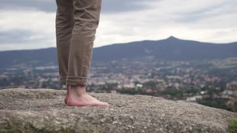 Closeup-of-male-barefoot-feet-walking-and-standing-on-rock-outside,-nice-background-of-nature-and-city
