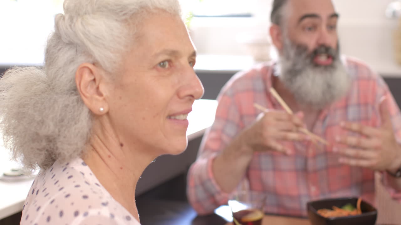 Smiling senior woman enjoying time with friend at home, sharing meal