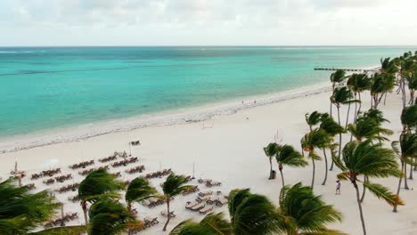 Windy-day-at-tropical-beach,-palm-trees-sway-in-strong-breeze,-turquoise-sea-and-tropical-coast-in-Dominican-Republic