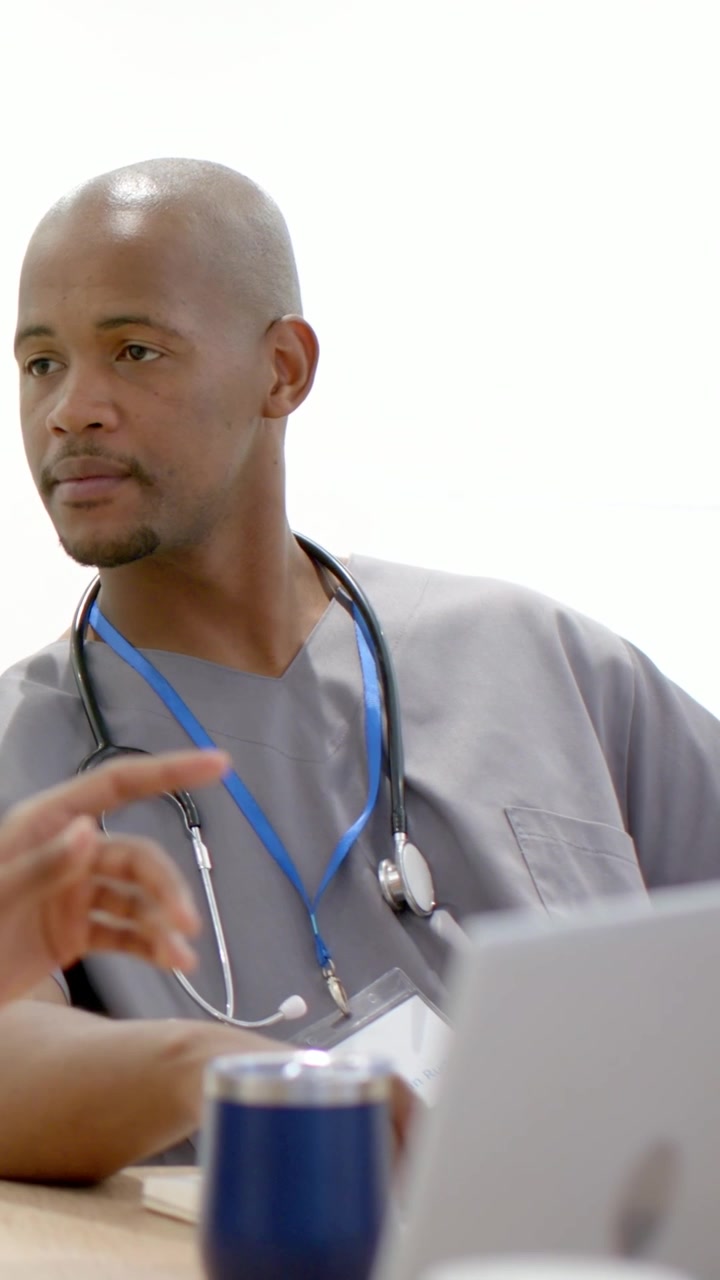 Video verticale: Infermiera in divisa che si gira seguendo il gesto della mano di un collega in clinica, con un laptop