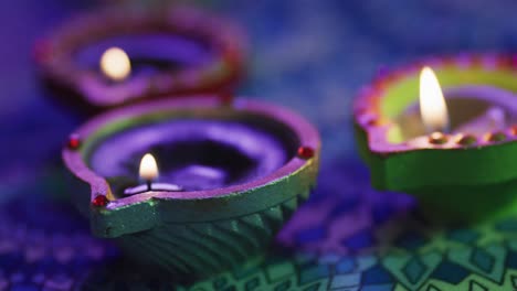 lit candles in decorative clay pots on patterned table top, focus on foreground, bokeh background