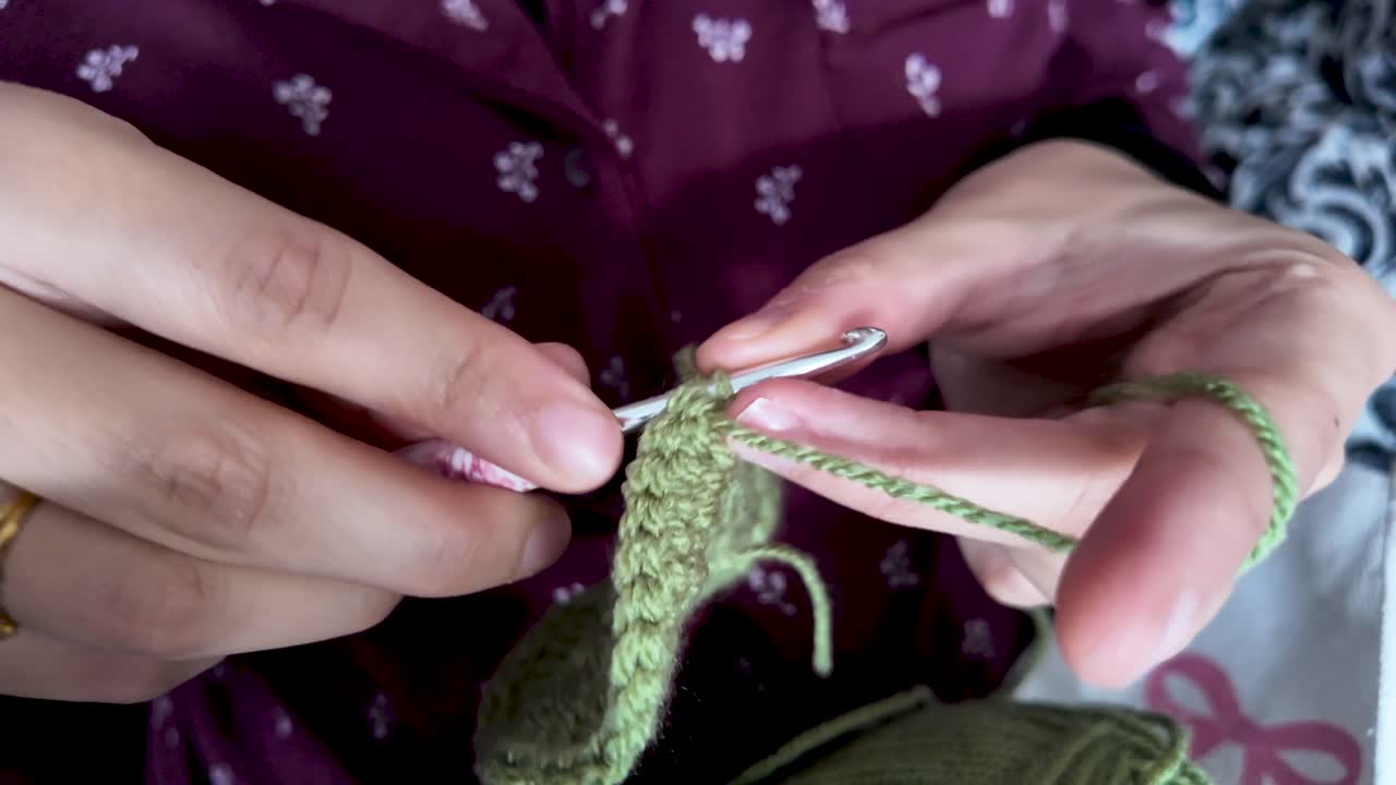 Primer plano de manos tejiendo ganchillo con hilo verde, elaborando proyectos textiles hechos a mano y pasatiempos creativos, tejiendo para el ocio y la relajación