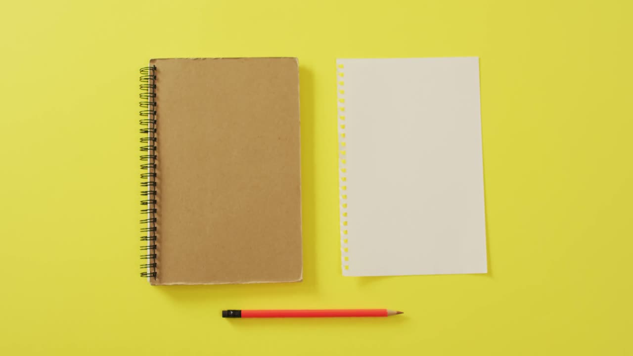 Video of notebook, empty sheet with copy space and pencil on yellow background