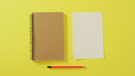 Video-of-notebook,-empty-sheet-with-copy-space-and-pencil-on-yellow-background