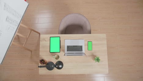 top view zoom out of a laptop next to the mock up green screen smartphone and tablet on the wooden desk besides a whiteboard at home