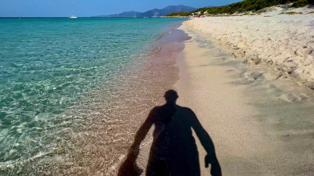 청록색 바닷물 해안선을 따라 모래 해변을 걷는 동안 모자를 벗는 남자의 실루엣 그림자