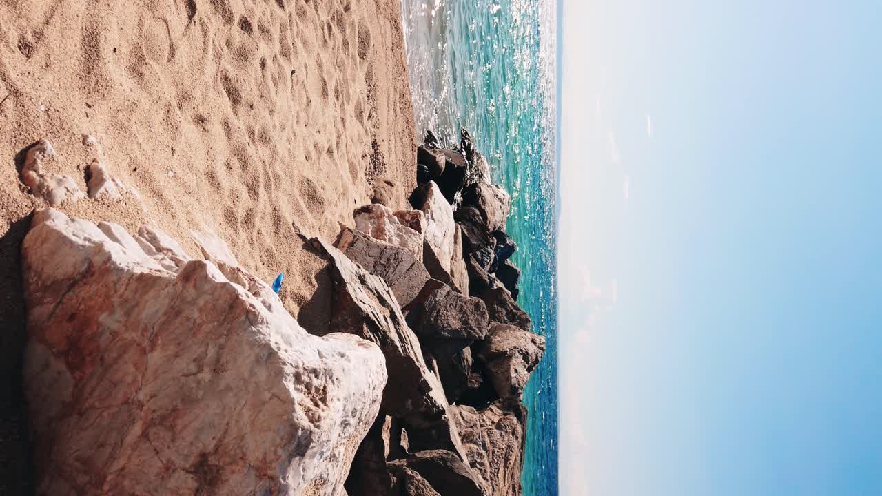 Beach on Aegean sea coast with rocks leading to the water, land in the distance in Nikiti, Greece. Slow motion, vertical shooting