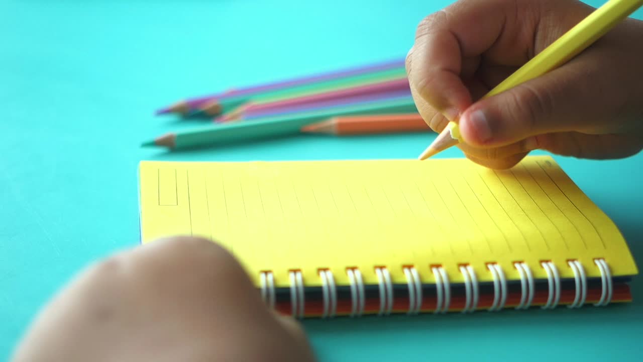 niño escribiendo en un cuaderno en espiral con lápices de colores