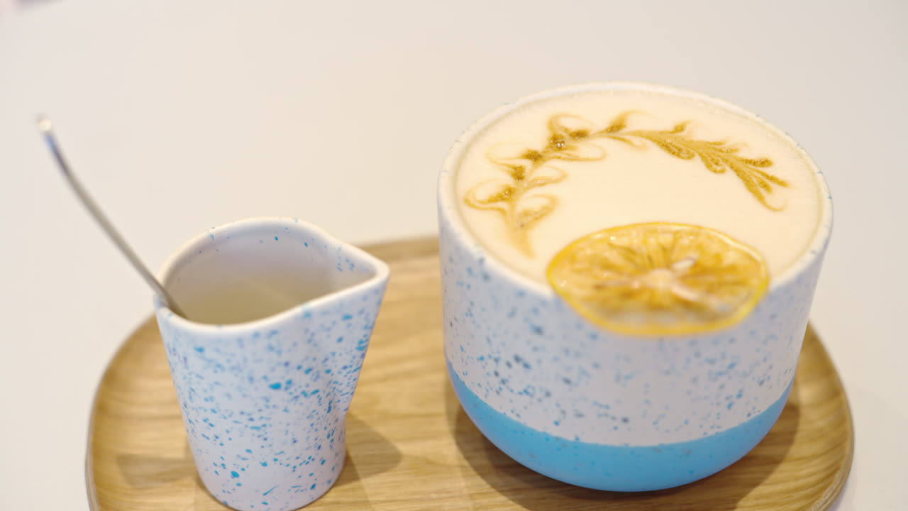 Latte art coffee in ceramic cup decorated with dry orange. Wooden plate