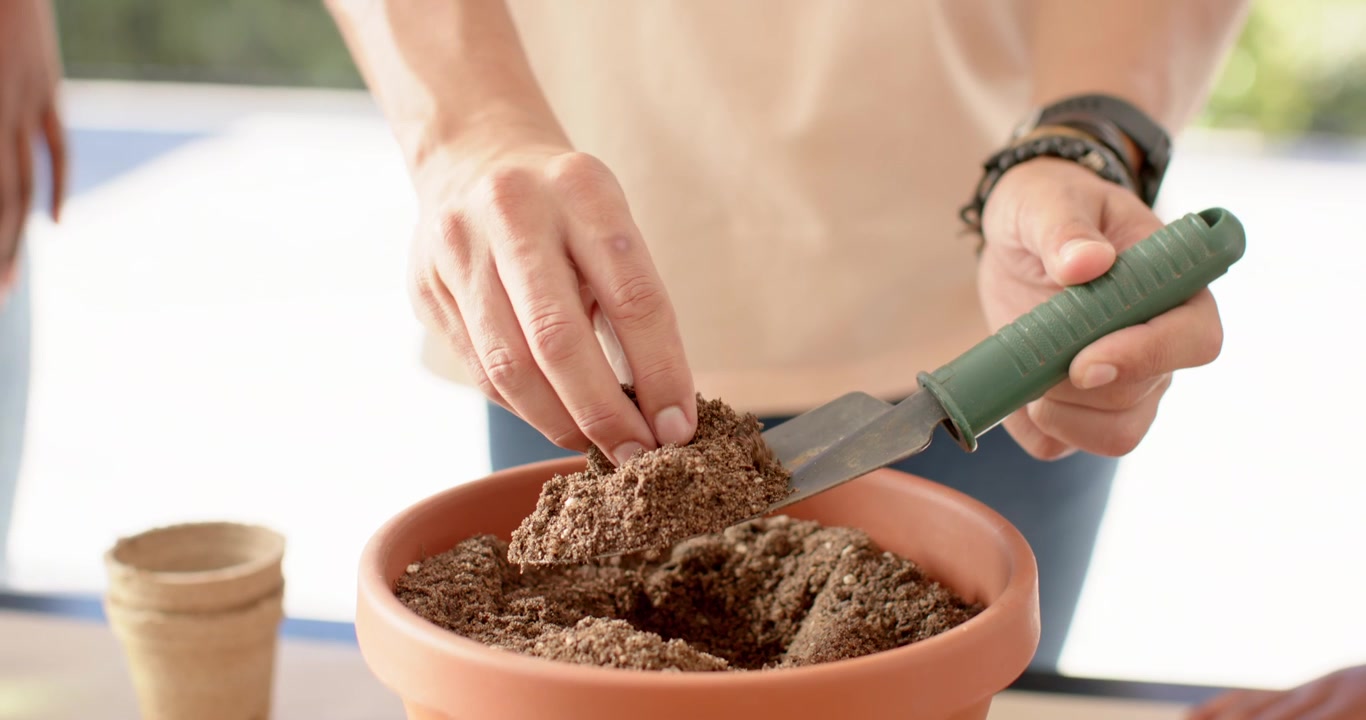 Amici afroamericani, un uomo che guida, che mette terra in un vaso di terracotta piantando semi per iniziare un giardino