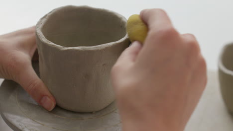 masterfully shaping clay into a cup using a turning wheel and sponge, a mesmerizing display of skill