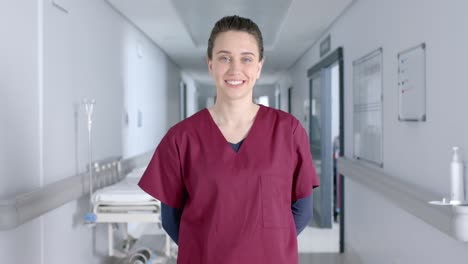 portrait of caucasian female doctor wearing scrubs, smiling in corridor, slow motion