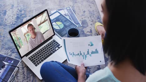 African-american-woman-holding-a-document-having-a-video-call-on-laptop-at-home