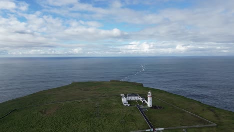 faro solitario en un cabo cubierto de hierba contra un vasto océano en la cabeza del bucle, vista aérea