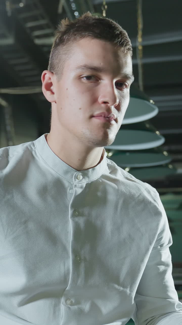 색 셔츠를 입고 약간 미소 짓는 남자가 희미하게 밝은 빌리어드 홀에서 큐 스틱을 들고 있는 클로즈업. 오버헤드 조명은 초록색 빌라 테이블에 반사를 던집니다. 자신감있는 표정은 집중과 전략을 암시합니다.