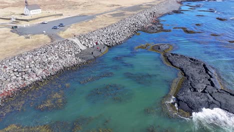 aerial footage near strandarkirkja church captures the dynamic scene of waves crashing against the shore