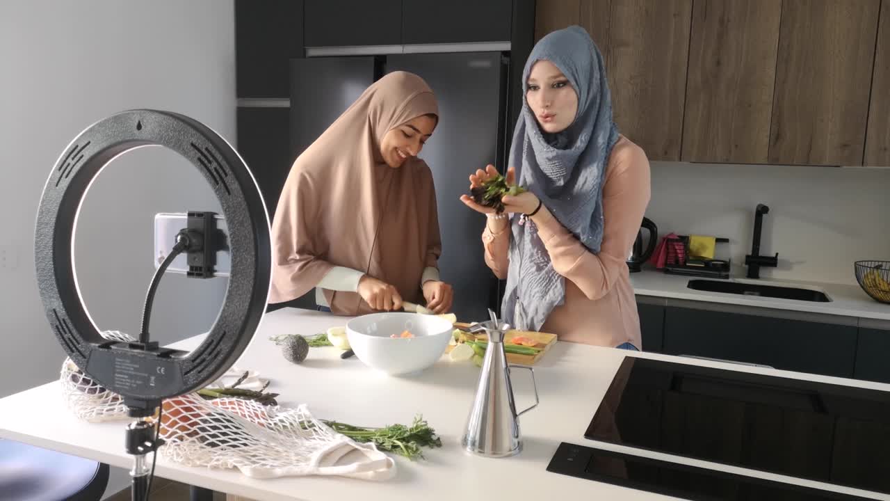 Two muslim food vloggers explaining how to prepare a salad at kitchen.
