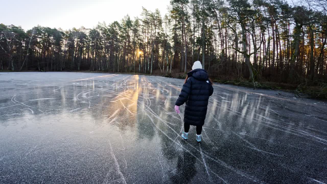 Slow-motion shot of a woman in a black jacket skating on black ice at sunrise