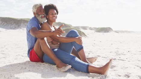 happy african american couple sitting and embracing on sunny beach