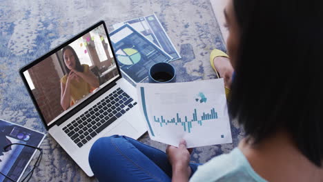 mujer afroamericana sosteniendo un documento haciendo una videollamada con una colega en una computadora portátil