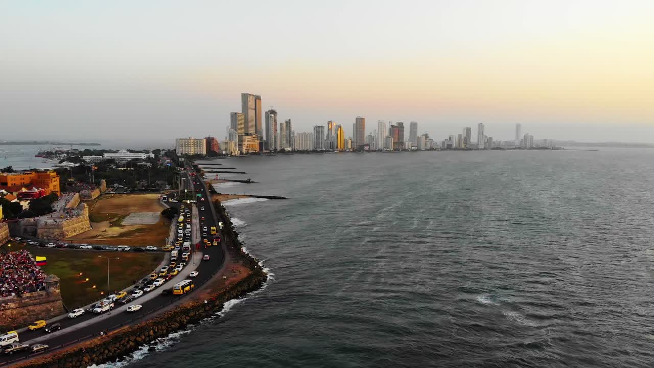 una toma aérea, ascendente, de un avión no tripulado del tráfico en la carretera de la avenida santader, el horizonte de cartagena en el fondo, durante la puesta de sol, en colombia