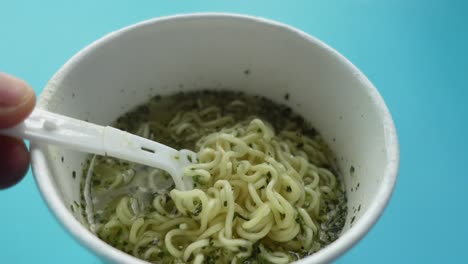 close-up view of a person eating instant noodles from a cup with a plastic fork