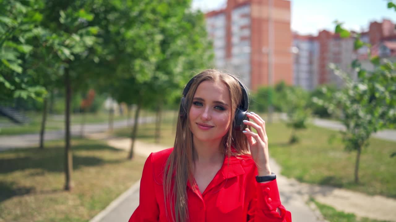 Lovely girl outdoors. Portrait of a young woman with headphones. Beautiful female listening to music in headphones on the city skyscrapers background.
