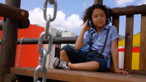 Vista-Frontal-De-Una-Colegiala-De-Raza-Mixta-Escuchando-Música-Con-Auriculares-En-El-Patio-De-La-Escuela-4k