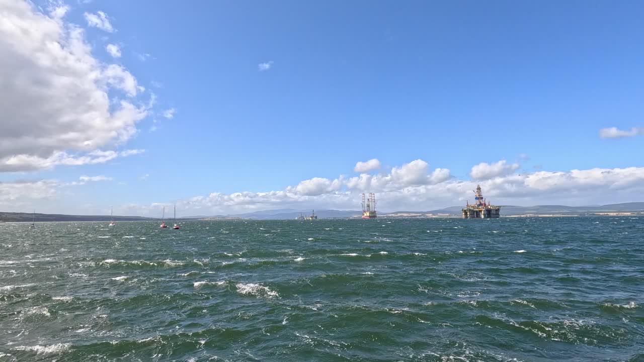 Multiple sailboats and fishing boats navigate rough sea waves under bright daylight and clear skies