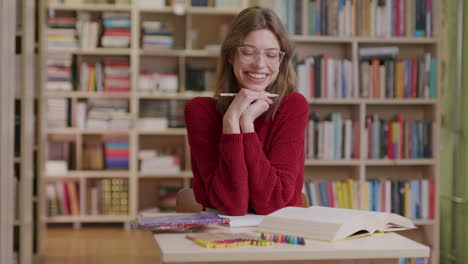 a young beautiful female student smiles into the camera while studying in the library—medium shot