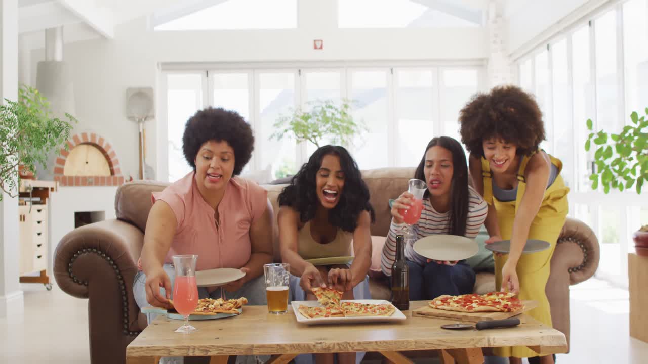 felices amigas diversas sentadas en el sofá en la sala de estar, comiendo pizza